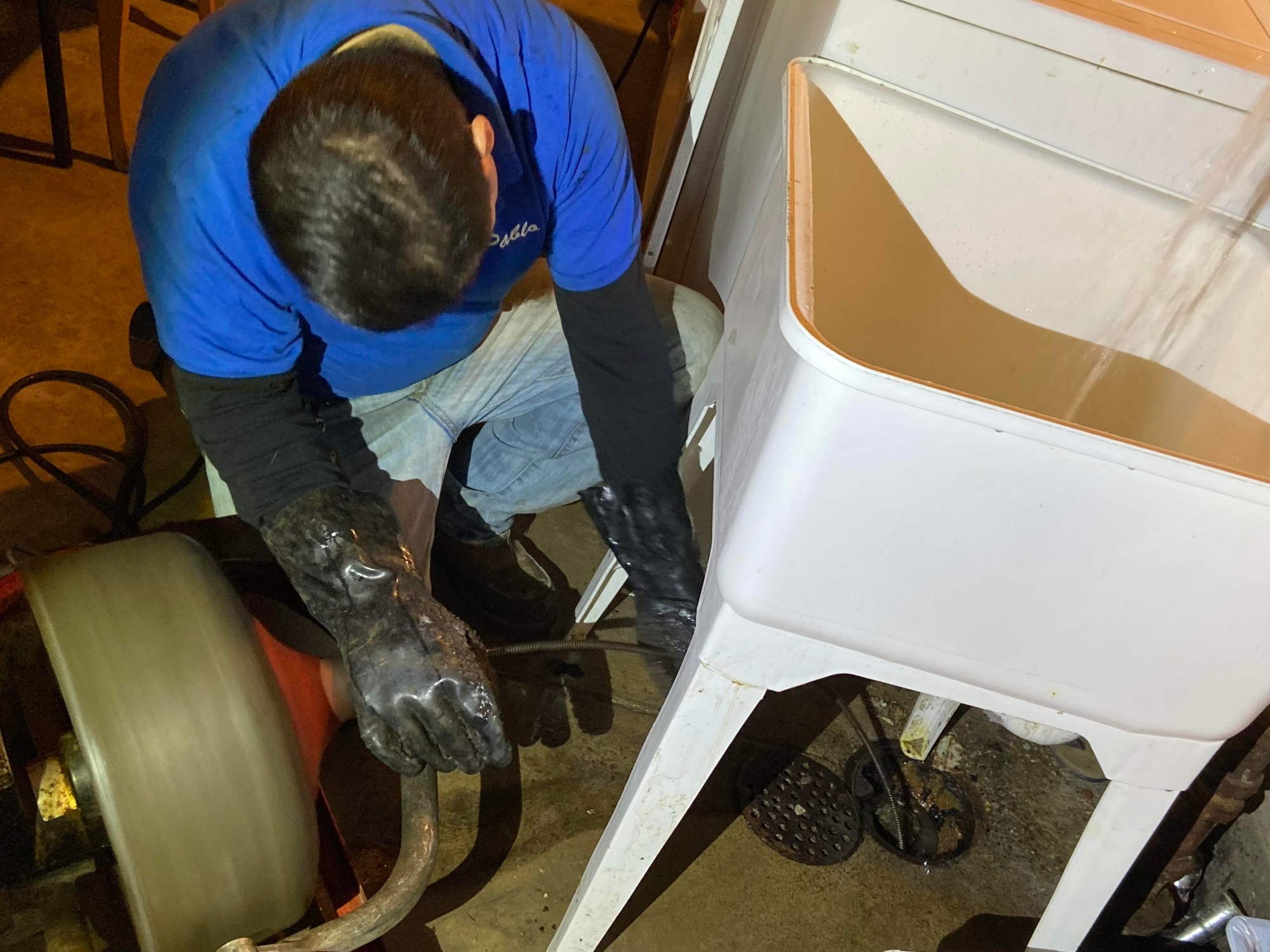 Technician snaking a basement floor drain beside a laundry sink