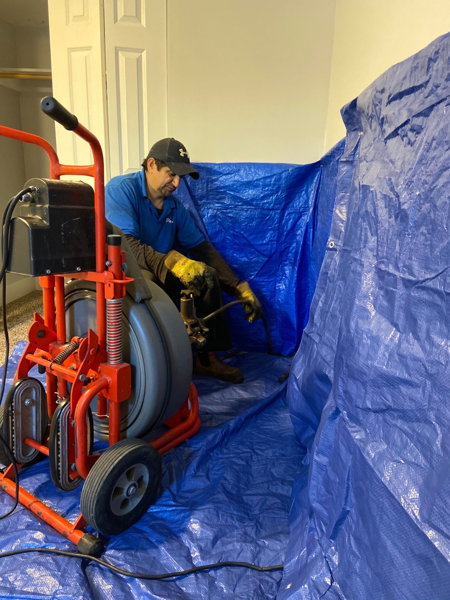 Technician running a drain machine with tarps laid down to protect the room